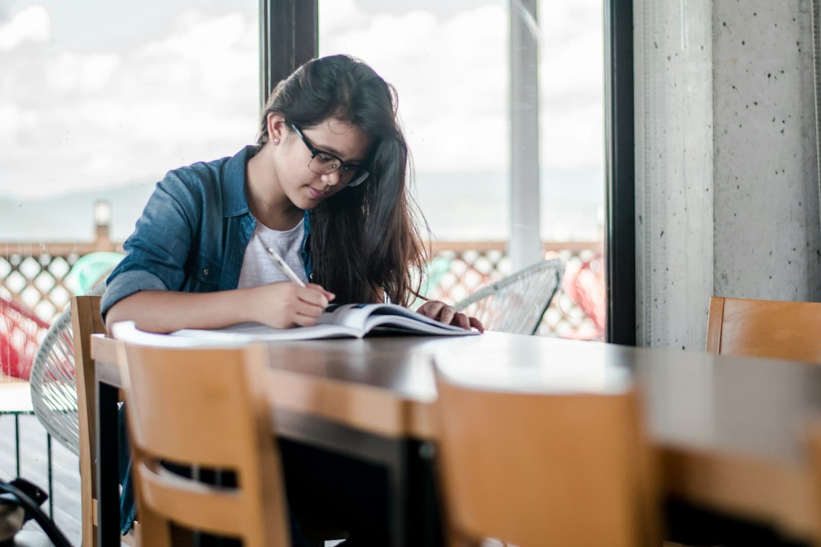 A student writing study notes at a table by the window